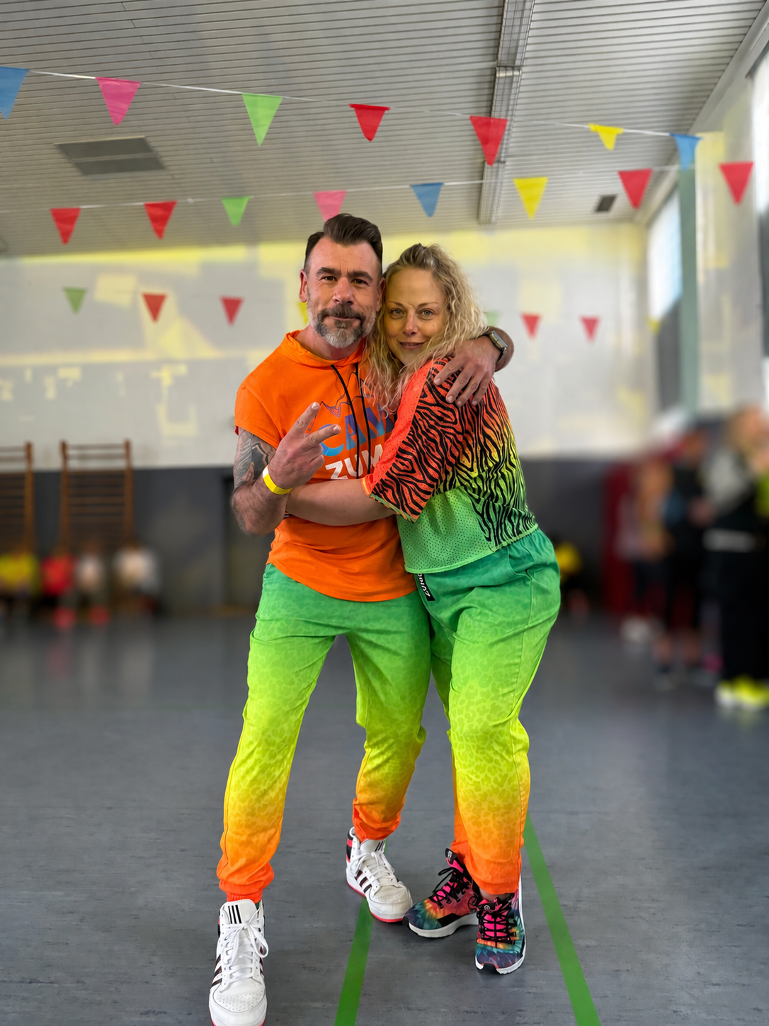 Daniela und Holger gemeinsam bei einem farbenfrohen Zumba-Event; Personen im Hintergrund sind unkenntlich